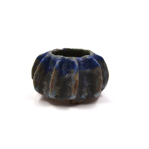 Puede incluir: Un pequeño cuenco de cerámica hecho a mano con un diseño texturizado único. El cuenco presenta un esmalte azul oscuro en el borde y las crestas exteriores, con un cuerpo moteado marrón y azul. El cuenco tiene una forma redondeada con un borde acanalado.