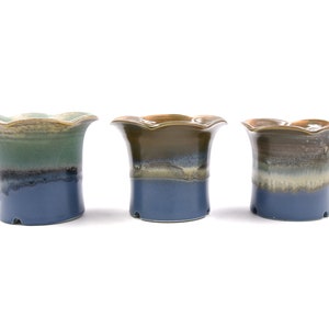 Op de afbeelding: Drie keramische bloempotten met een gegolfde rand. De potten zijn geglazuurd in tinten blauw, groen, bruin en beige.
