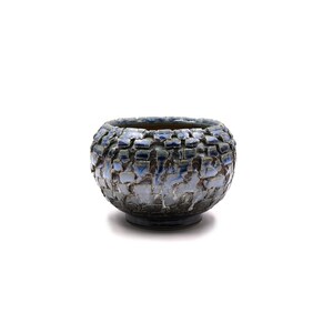 May include: A round ceramic bowl featuring a textured, block-like surface pattern. The exterior displays a gradient of deep charcoal gray at the base transitioning into a mottled, icy blue and white glaze across the upper sections and rim.