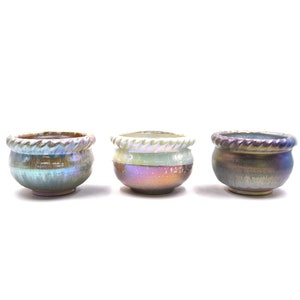 Pode incluir: Três pequenos vasos de cerâmica com esmalte iridescente em tons de verde, marrom e roxo. Os vasos têm um design de corda ao redor da borda.