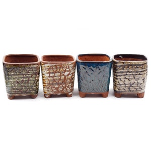 May include: Four square ceramic planters with different glaze patterns. The planters are brown, green, blue, and white with a textured finish. Each planter has four small feet.