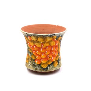 Könnte beinhalten: Eine Keramikvase mit breitem, ausgestelltem Rand und strukturierter Außenseite. Die Vase ist mit einem lebendigen Design aus orangefarbenen Beeren und gelben Blättern auf dunklem Hintergrund verziert. Der Innenraum ist in einem warmen Terrakotta-Ton gehalten.