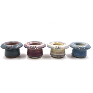 May include: Four ceramic egg cups in the shape of top hats. The egg cups are decorated with a white and blue glaze, a white and purple glaze, a white and yellow glaze, and a white and blue glaze.