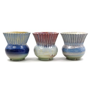 Pode incluir: Três vasos de cerâmica com um design texturizado e canelado. Os vasos são envidraçados em tons de azul, vermelho e branco.