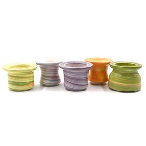 May include: Six colorful, handmade ceramic candle holders. Each holder has a unique swirl pattern in shades of yellow, purple, orange, and green. The holders are approximately 3 inches tall and have a wide, flat base.