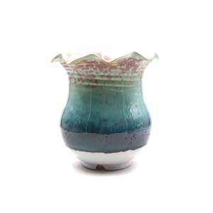 Puede incluir: Un jarrón de cerámica con un borde festoneado y un esmalte azul, verde y blanco. El jarrón tiene un diseño moteado y una base blanca.