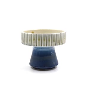 May include: A ceramic pedestal with a white and blue glaze. The top of the pedestal is a wide, shallow bowl with a textured rim.