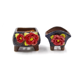 May include: Two blue and brown ceramic flower pots with red and yellow flower designs. The pots have four legs each.