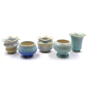 以下が含まれることがあります： さまざまな形と色の6つの小さなセラミック花瓶のコレクション。花瓶は、ライトブルー、クリーム、イエローなど、さまざまなパステルカラーが特徴です。各花瓶はユニークなデザインで、フリルエッジのあるものもあります。