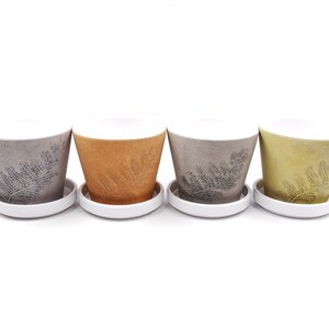 May include: Four ceramic plant pots with white saucers. The pots are in different colors: gray, orange, brown, and yellow. Each pot has a fern design.