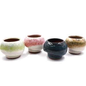 May include: Four ceramic mushroom-shaped planters in various colors. The planters have a rounded top and a flared base. Colors include green, pink, blue, and gold. The interiors are a dark brown color.