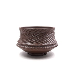 Può includere: Un vaso in ceramica marrone con un design testurizzato e ondulato. Il vaso ha una base larga e un'apertura stretta.