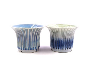 May include: Two ceramic planters with a blue and white glaze. The planters have a fluted design and a wide, shallow base.