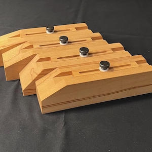 May include: Four wooden clamps with black knobs and white plastic inserts. The clamps are stacked on top of each other.