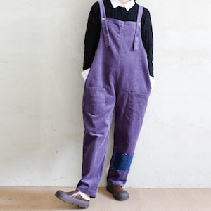 May include: Purple corduroy overalls with a patch on the left leg. The overalls have two pockets on the front and adjustable straps.