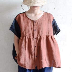 May include: A rust-coloured linen blouse with black short sleeves and a button-up front. The blouse has a gathered waist and a slightly flared hem.