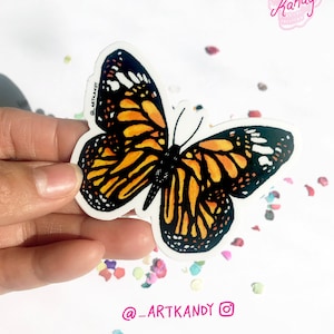 May include: A sticker featuring a monarch butterfly with black, orange, and white wings. The sticker is on a white background with colorful confetti.