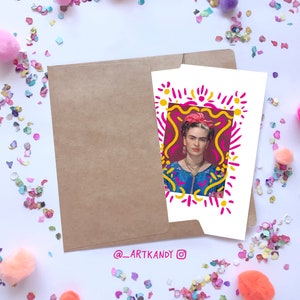 May include: A white card with a colorful illustration of Frida Kahlo in a frame. The frame is made of pink, yellow, and orange lines. The background is a dark red color. The card has the text "@_artkandy_" at the bottom.