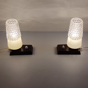 May include: Two vintage bedside lamps with white frosted glass shades and black bases. The shades have a diamond pattern and the lamps are turned on.