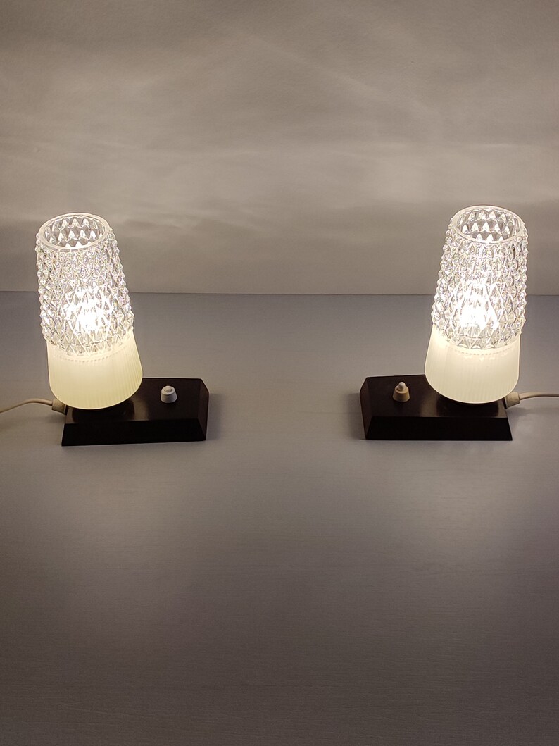 May include: Two vintage bedside lamps with white frosted glass shades and black bases. The shades have a diamond pattern and the lamps are turned on.