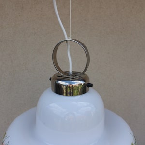 以下が含まれることがあります： 白いガラス製のペンダントライトのクローズアップ。クロムメッキの金属製の吊り下げリングとクロムメッキの金属製のキャノピーが付いています。照明器具は花柄です。