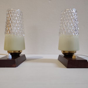 May include: Two vintage table lamps with textured glass shades and wooden bases. The lamps have a white cord and a white switch.