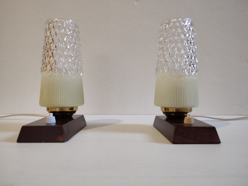 May include: Two vintage table lamps with textured glass shades and wooden bases. The lamps have a white cord and a white switch.