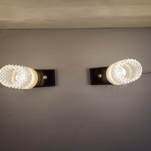 May include: Two white glass wall sconces with a textured design, each mounted on a black rectangular base.