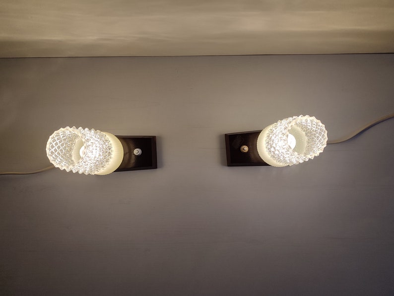 May include: Two white glass wall sconces with a textured design, each mounted on a black rectangular base.