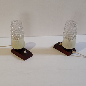 May include: Two vintage table lamps with clear glass shades and brown wooden bases. Each lamp has a white cord and a white switch.