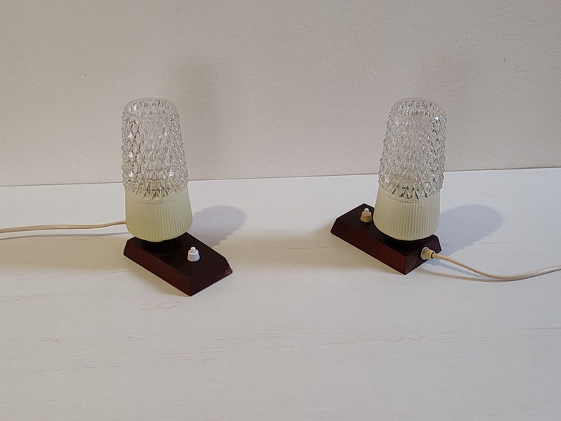 May include: Two vintage table lamps with clear glass shades and brown wooden bases. Each lamp has a white cord and a white switch.