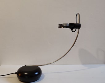 May include: A black and silver desk lamp with a curved arm and a round base. The lamp has a circular light fixture with multiple layers.