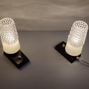 May include: Two vintage bedside lamps with clear glass shades and black bases. The lamps have a white cord and a switch on the base.