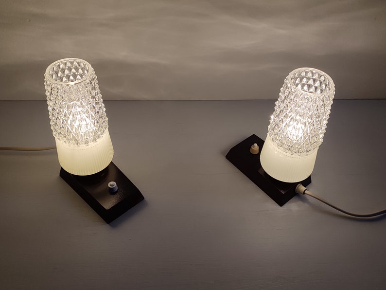 May include: Two vintage bedside lamps with clear glass shades and black bases. The lamps have a white cord and a switch on the base.