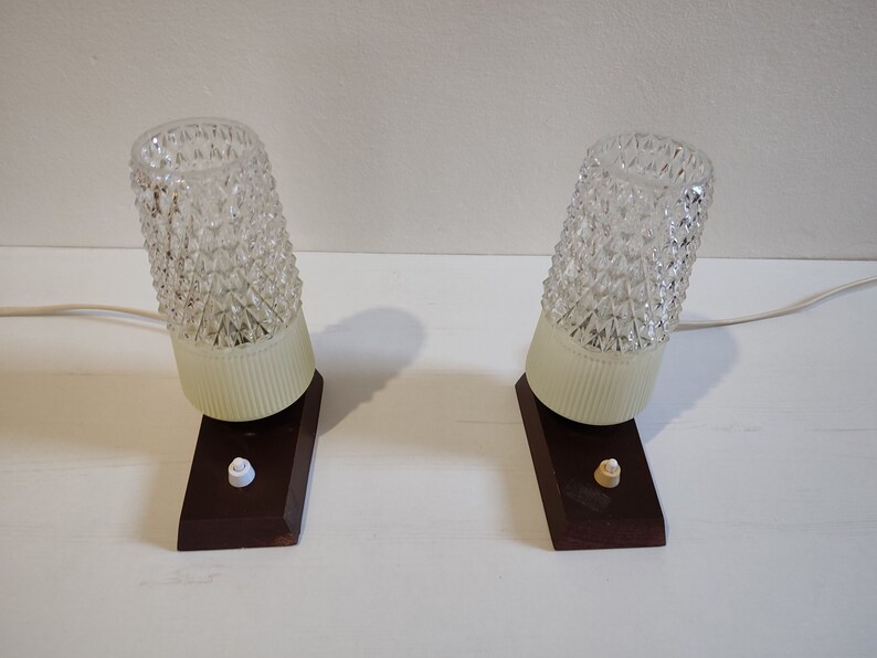 May include: Two vintage table lamps with clear glass shades featuring a diamond pattern. The lamps have a white base and a brown wooden base with a white switch.