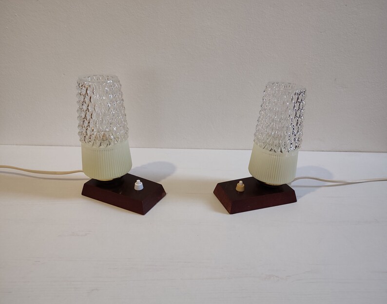 May include: Two vintage table lamps with clear glass shades and brown wooden bases. Each lamp has a white plastic shade and a small white switch.