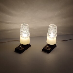 May include: Two white glass table lamps with a diamond pattern on the shade. The lamps are on a black base and have a cord.