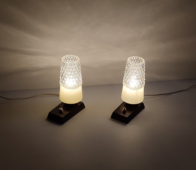 May include: Two white glass table lamps with a diamond pattern on the shade. The lamps are on a black base and have a cord.