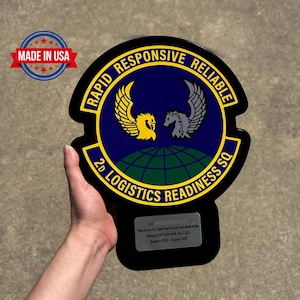 May include: A black plaque with the words "RAPID RESPONSIVE RELIABLE" and "2D LOGISTICS READINESS SQ." The plaque features a yellow and gray winged emblem over a blue background. The text "MADE IN USA" is also visible.