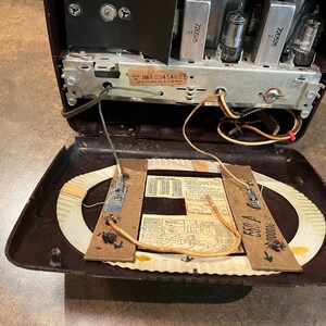 May include: Inside view of a vintage brown radio with the back panel open, revealing the internal components, including a circular antenna, wires, and a label with the serial number "5M10945468".