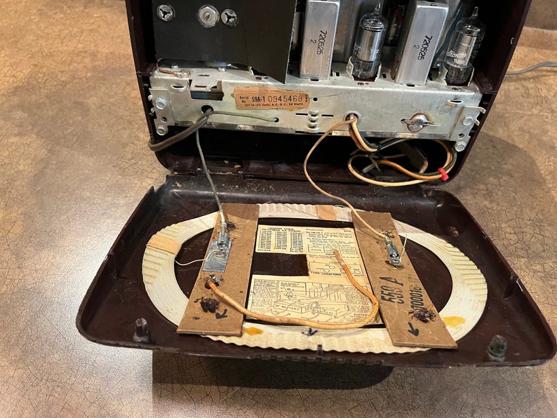 May include: Inside view of a vintage brown radio with the back panel open, revealing the internal components, including a circular antenna, wires, and a label with the serial number "5M10945468".