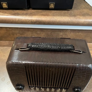 May include: A brown vintage radio with a black leather handle and a crocodile-embossed design. The radio has a dial with numbers from 55 to 180.