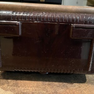May include: A dark brown vintage radio with a textured top and two small rectangular openings on the back.