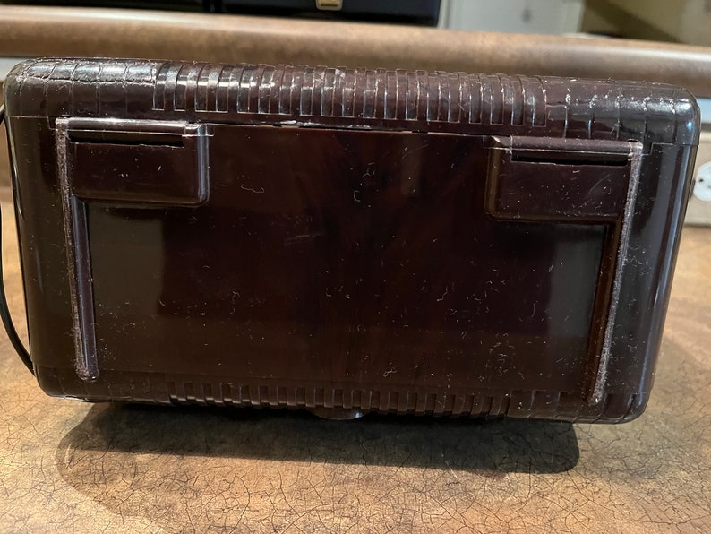 May include: A dark brown vintage radio with a textured top and two small rectangular openings on the back.