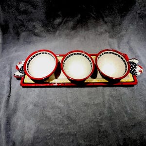 May include: A decorative serving tray with three white bowls, each with a red rim and black and white polka dots. The tray is red with yellow and black accents and has decorative chicken-themed handles.