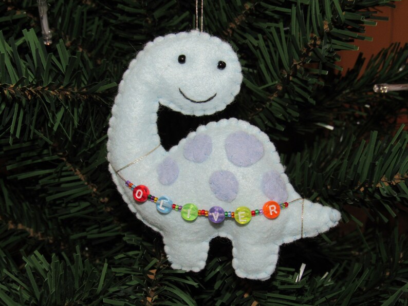 May include: A light blue felt dinosaur ornament with purple spots and a beaded necklace that spells "Oliver".