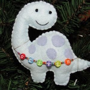 May include: A light blue felt dinosaur ornament with purple spots and a beaded necklace spelling "Oliver".