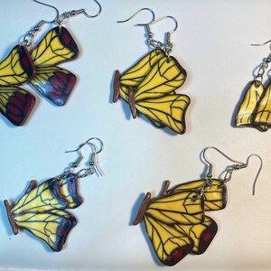 Könnte beinhalten: Vier Paar Schmetterlings-Ohrringe mit gelben und roten Flügeln. Die Ohrringe sind aus Polymer Clay gefertigt und haben silberne Haken.