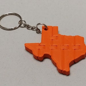 May include: Orange plastic keychain shaped like the state of Texas. The keychain is made of interlocking pieces and has a silver metal key ring.