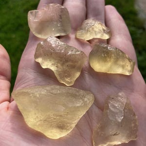 Puede incluir: Seis piezas de vidrio de mar amarillo, cada una con una forma y textura únicas, se muestran en una mano. El vidrio de mar es translúcido y tiene un aspecto ligeramente nublado.